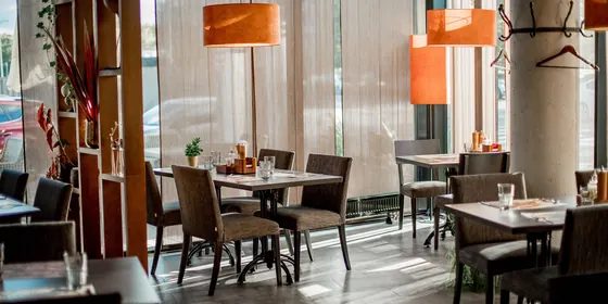 Sală de restaurant cu mese aranjate și ferestre de la podea la tavan