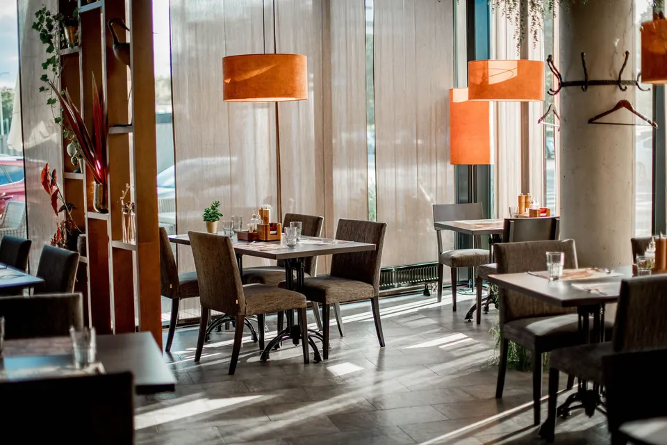 Sală de restaurant cu mese aranjate și ferestre de la podea la tavan